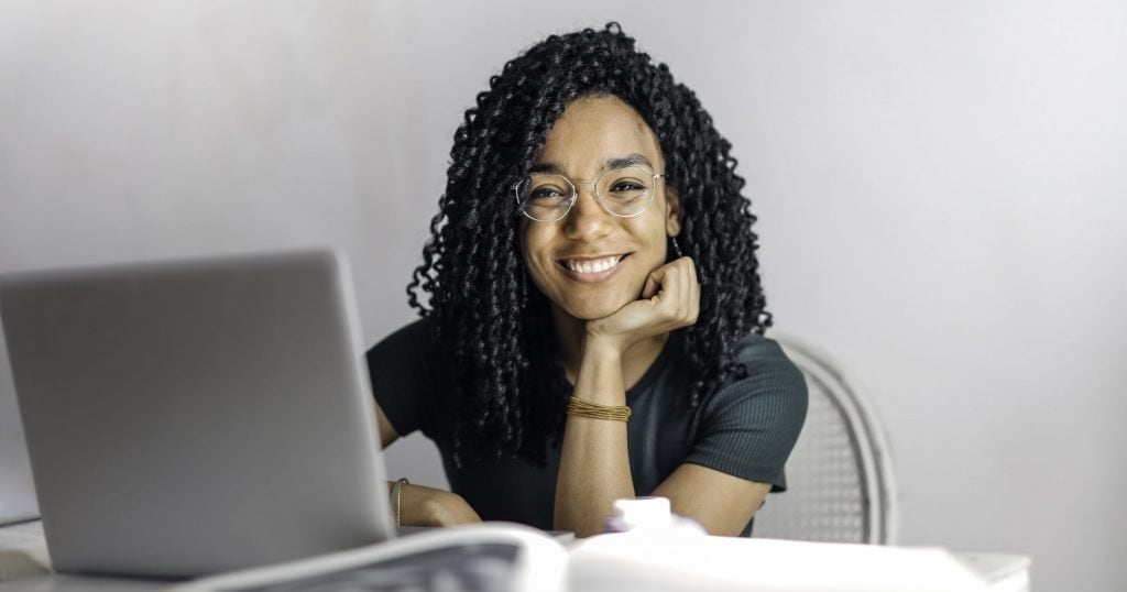 Happy ethnic woman sitting at table with laptop