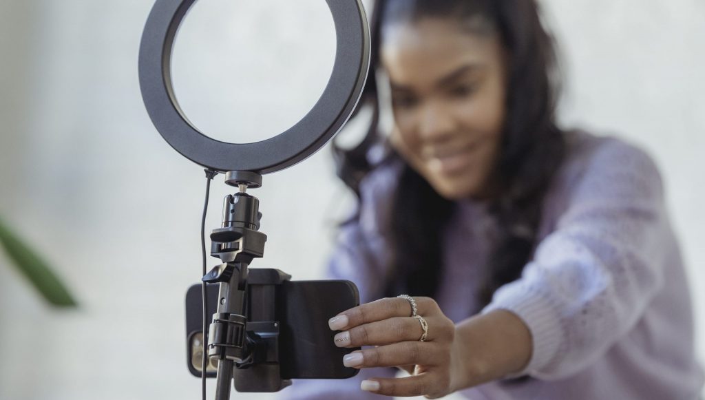 Happy young black woman setting up smartphone before shooting podcast