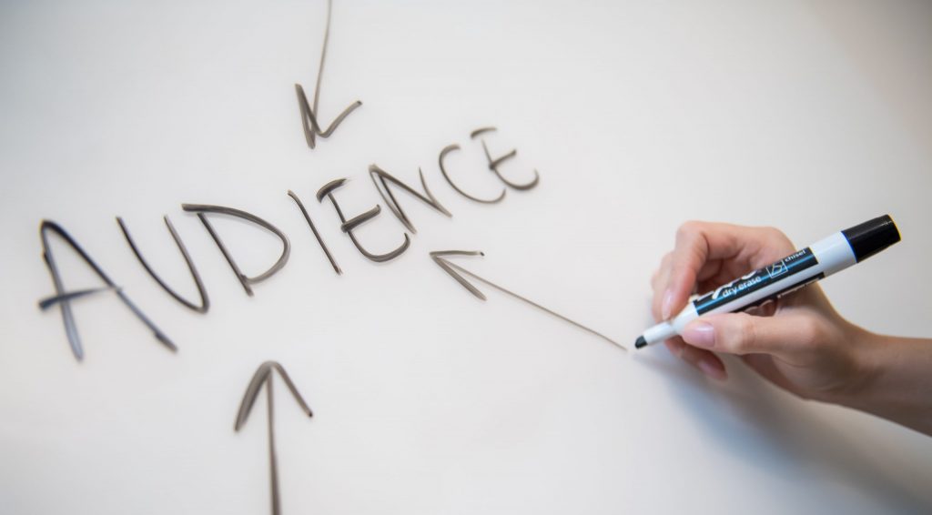 Woman's hand writing the word "audience" on a whiteboard, with arrows.