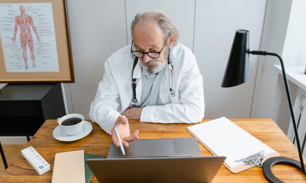 An elderly doctor looking at the monitor of a laptop