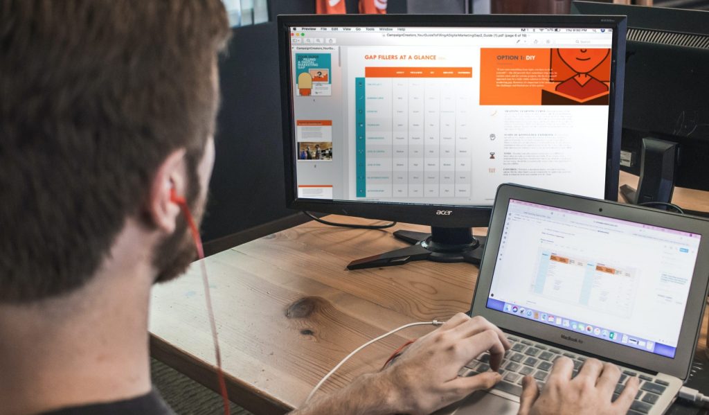 man wearing red earphone sitting on chair while using laptop