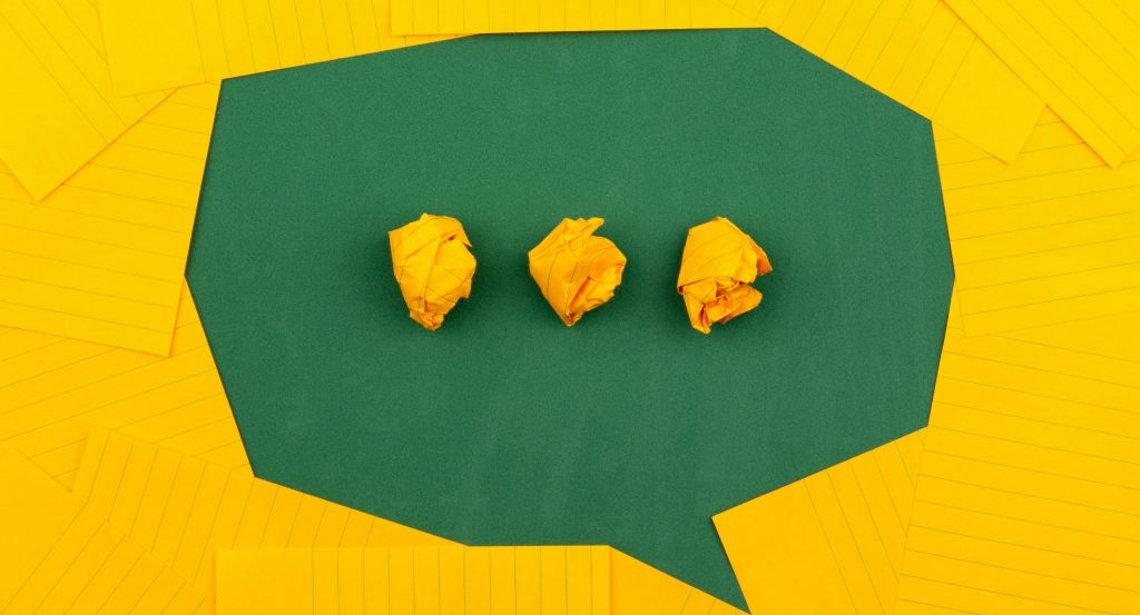 orange sheets of paper lie on a green school board and form a chat bubble with three crumpled papers.