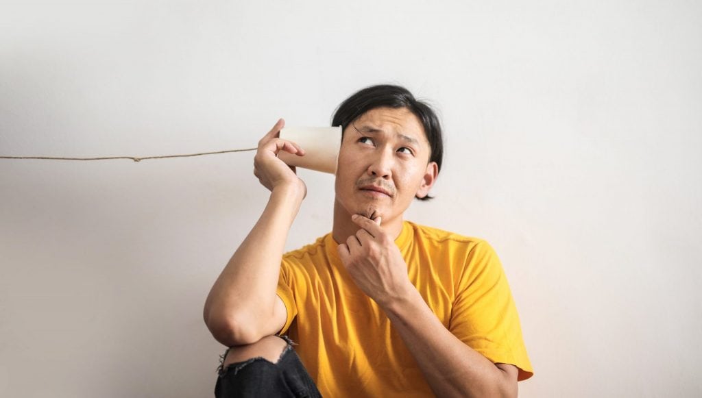 Pensive ethnic man listening to answer in paper cup phone