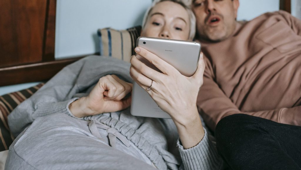 Relaxed multiethnic couple lying on bed and watching video on tablet