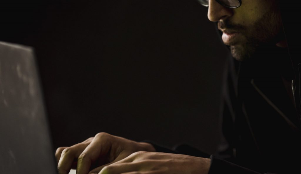 Crop bearded man working on laptop in darkness