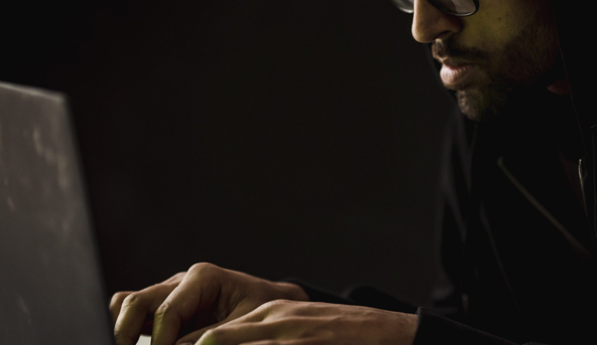 Crop bearded man working on laptop in darkness