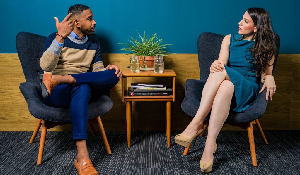 Woman wearing teal dress sitting on chair talking to man